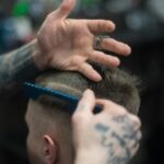 Close-up of a tattooed barber giving a stylish haircut indoors, highlighting modern grooming techniques.